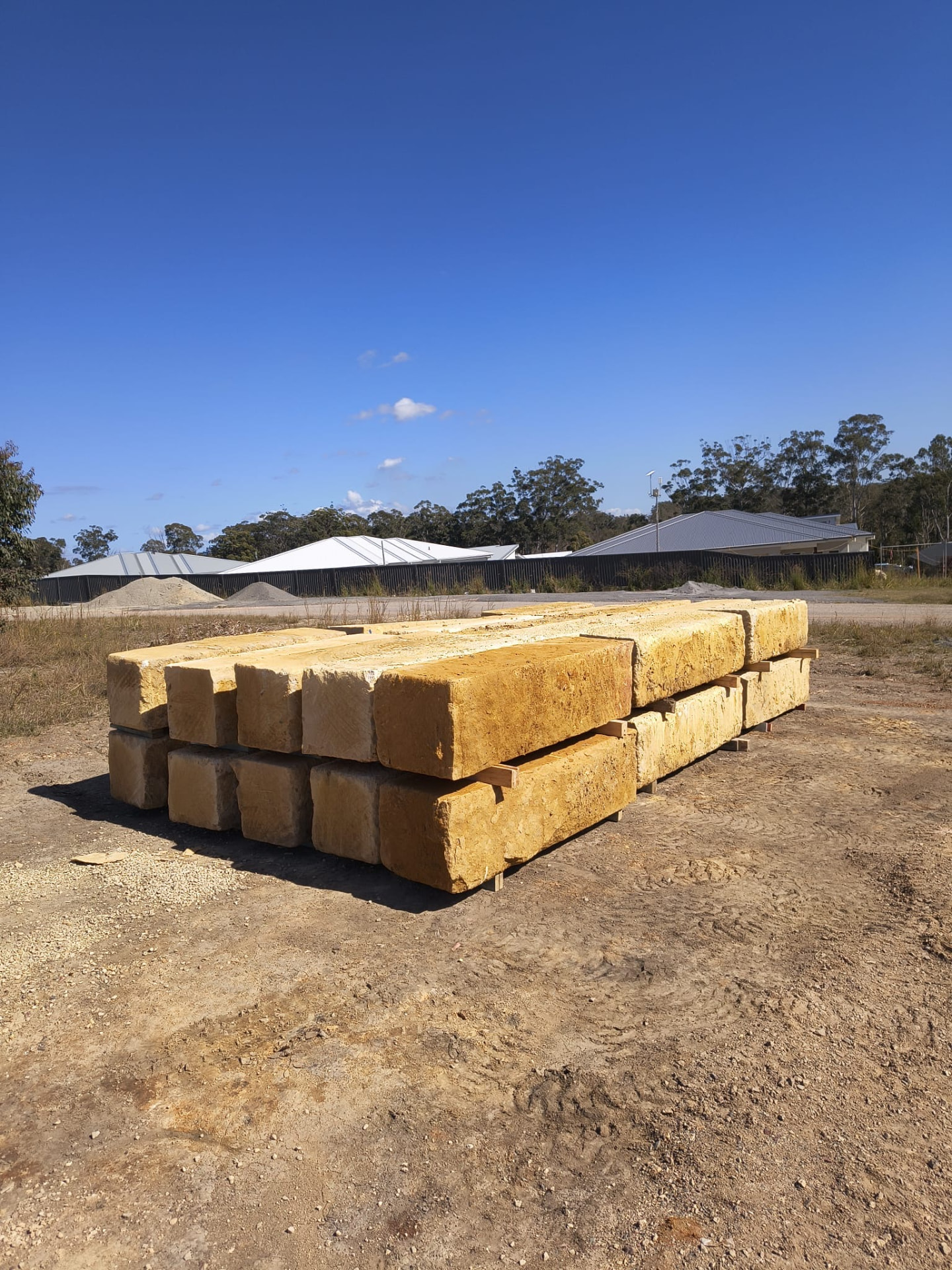 Stacked sandstone logs in the Get Stones yard under clear blue sky