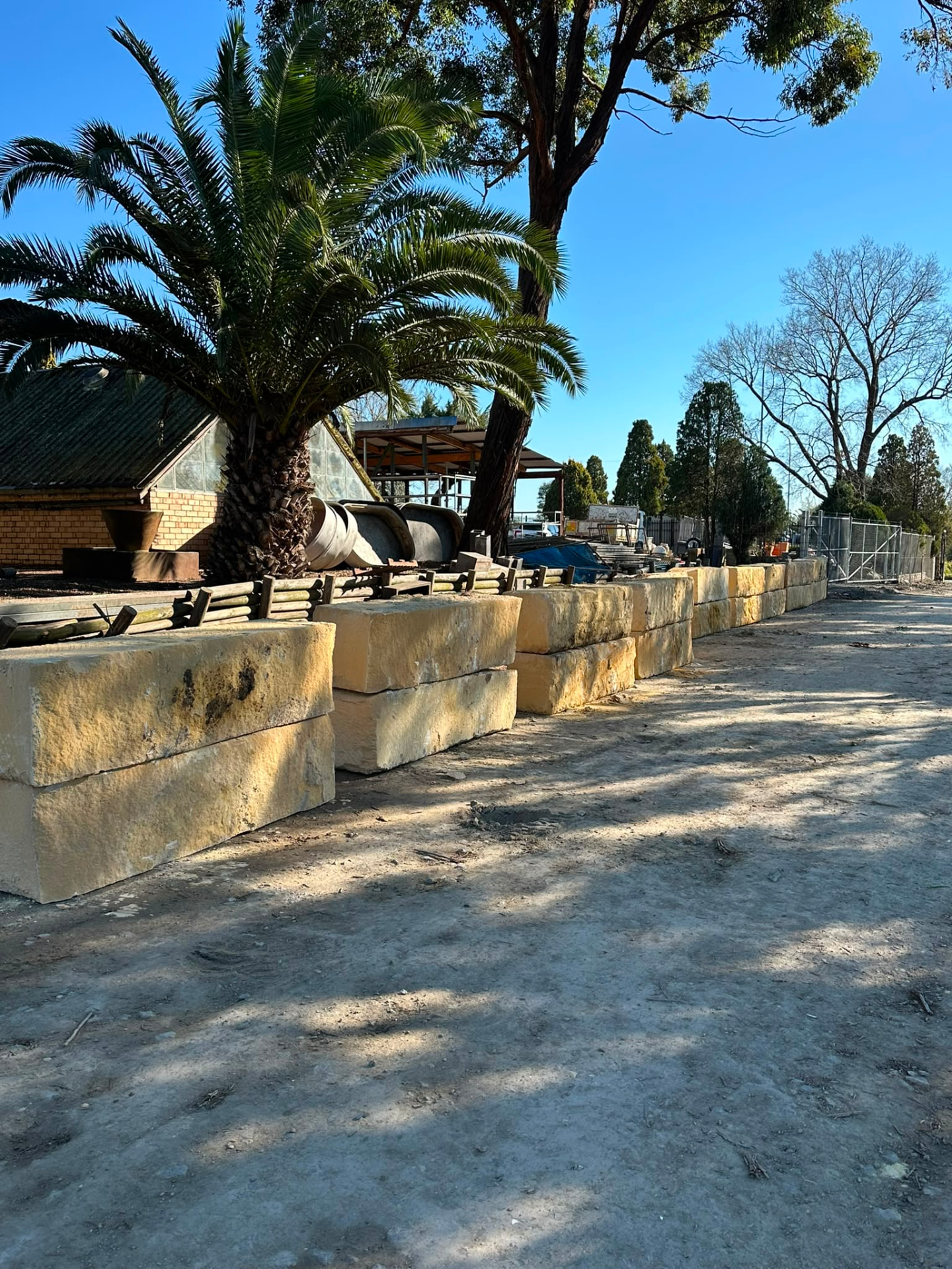 Sandstone block retaining wall running alongside a palm-lined garden bed